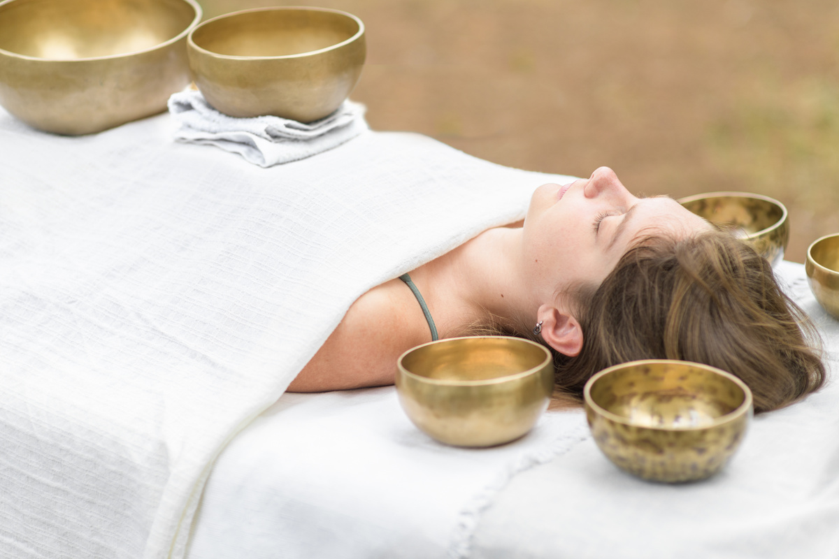 Young woman laying on a massage bed with tibetan singing bowl outdoor. Nepal copper singing bowl sound massage